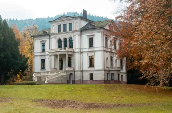 Grande demeure de caractère à façade blanche entourée d’un parc arboré.