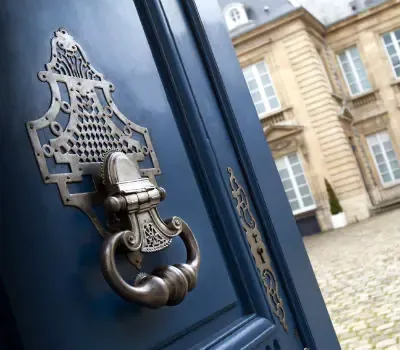 Porte bleue ornée d’un heurtoir devant la façade d’une demeure de prestige.