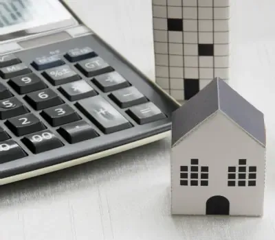 Calculatrice posée à côté d’une maquette de maison sur une surface claire.
