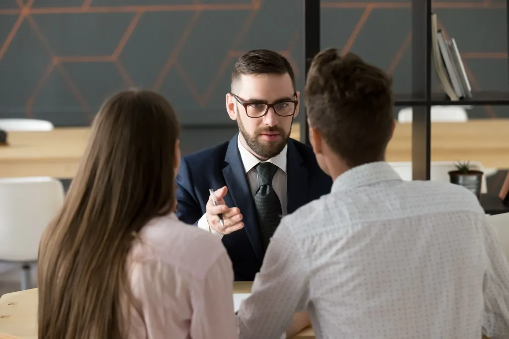 Expert en costume échangeant avec un couple autour d’une table dans un bureau contemporain.