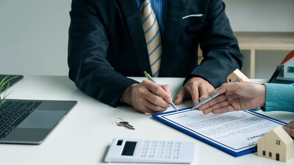 Professionnels examinant un dossier d’expertise immobilière avec une calculatrice et des maquettes de maisons.