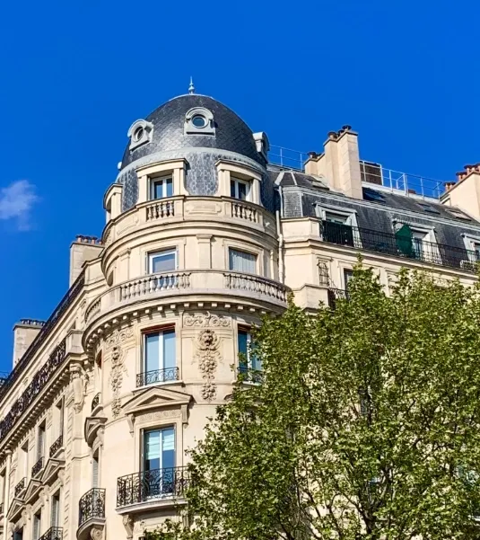 Façade ornée d’un immeuble ancien à rotonde et toiture en ardoise.