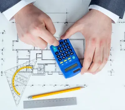 Deux mains calculent une évaluation immobilière sur le plan d’un appartement avec une calculatrice.