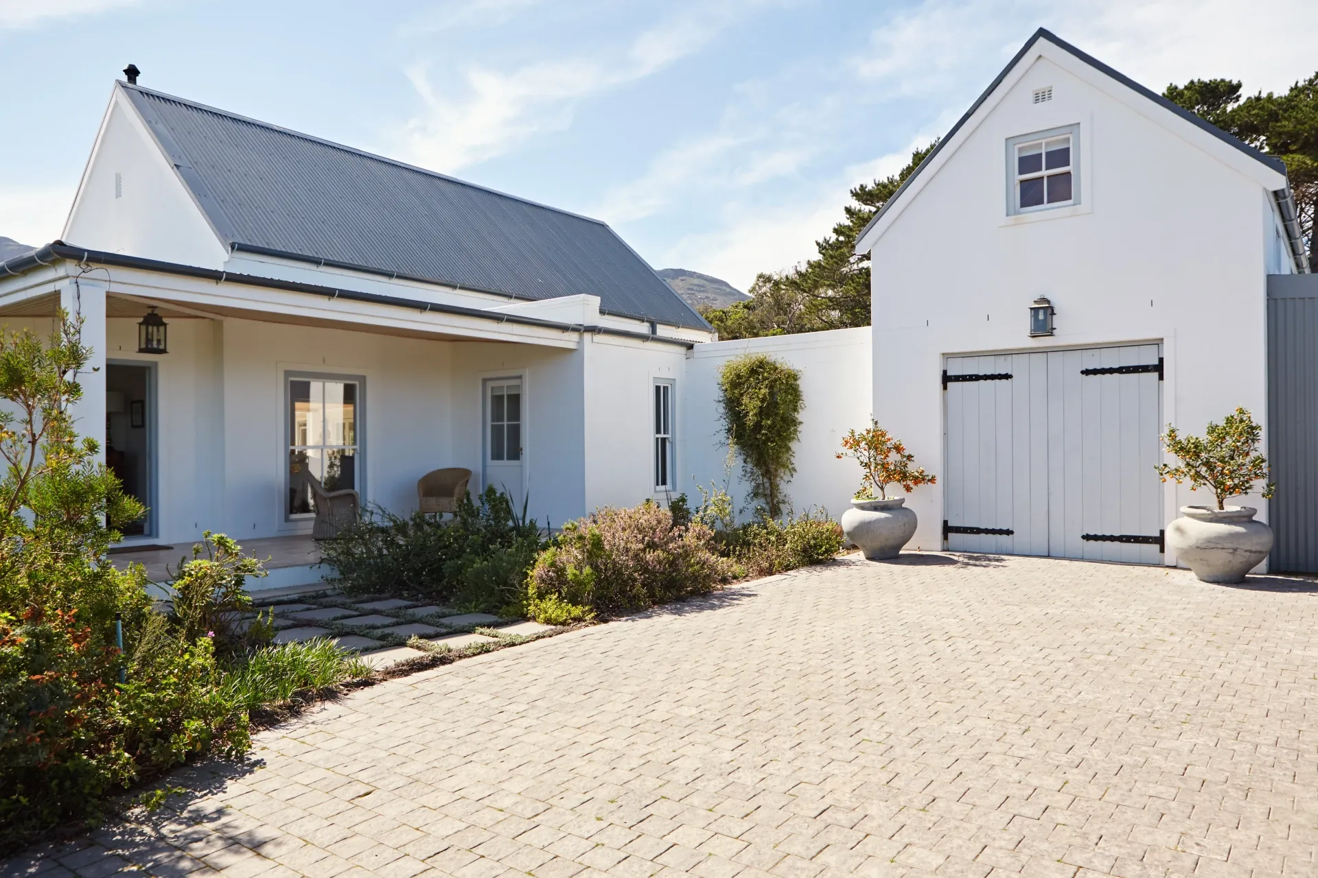 Vue extérieure d’une maison résidentielle blanche avec jardin et allée pavée.