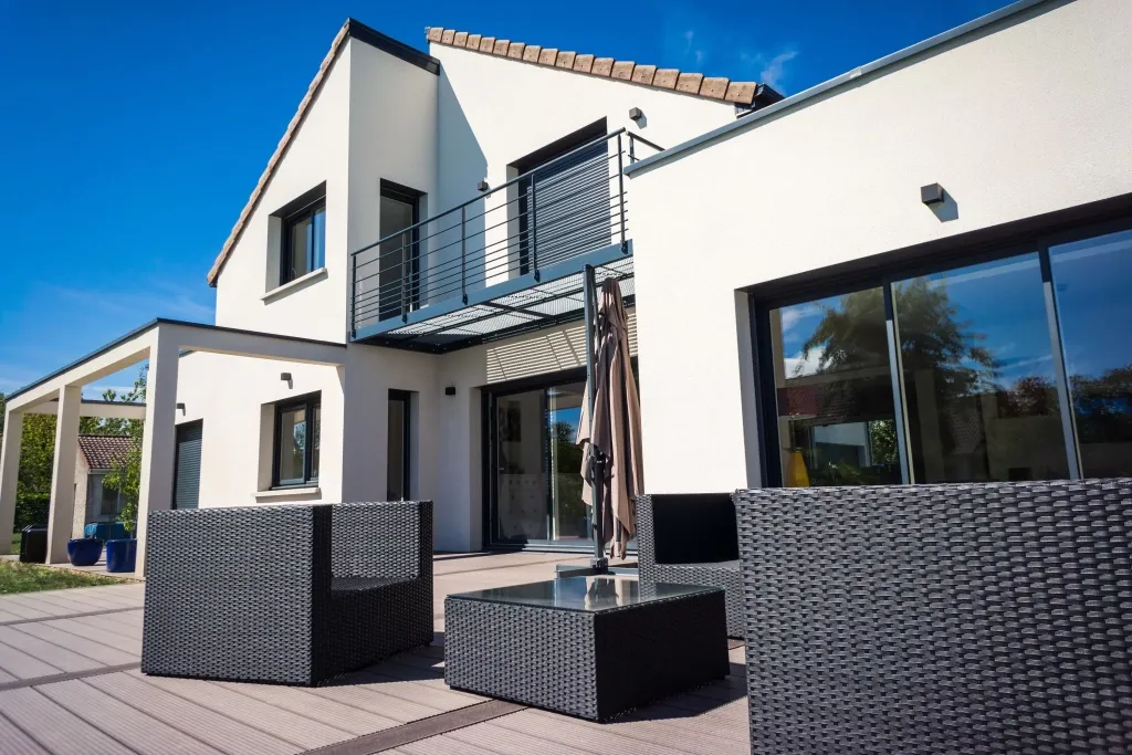 Maison contemporaine aux façades blanches avec terrasse aménagée et mobilier extérieur.