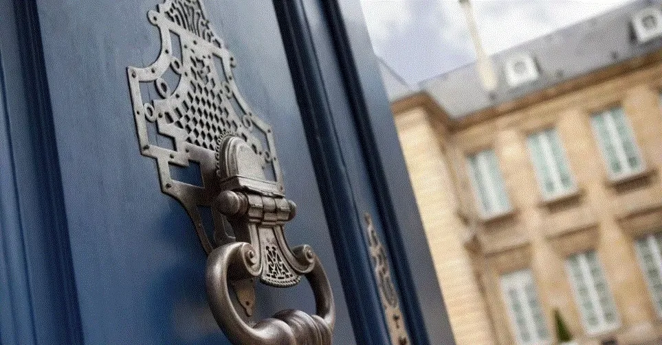 Gros plan sur un heurtoir ouvragé fixé à une porte bleu foncé devant une façade ancienne.
