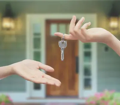 Deux mains échangent les clés d’une maison devant son entrée.